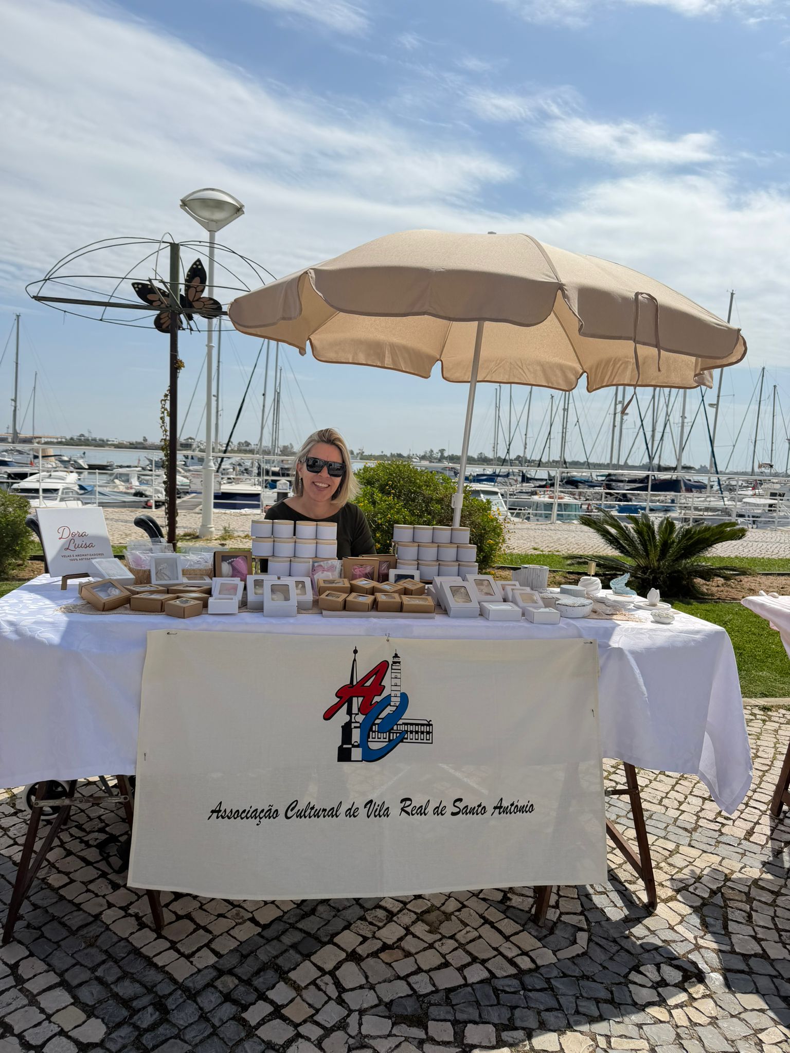 A Dora Luísa sorridente atrás da banca montada na marina de Vila Real de Santo António